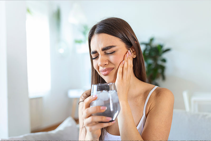 person holding their mouth and jaw in pain while drinking water
