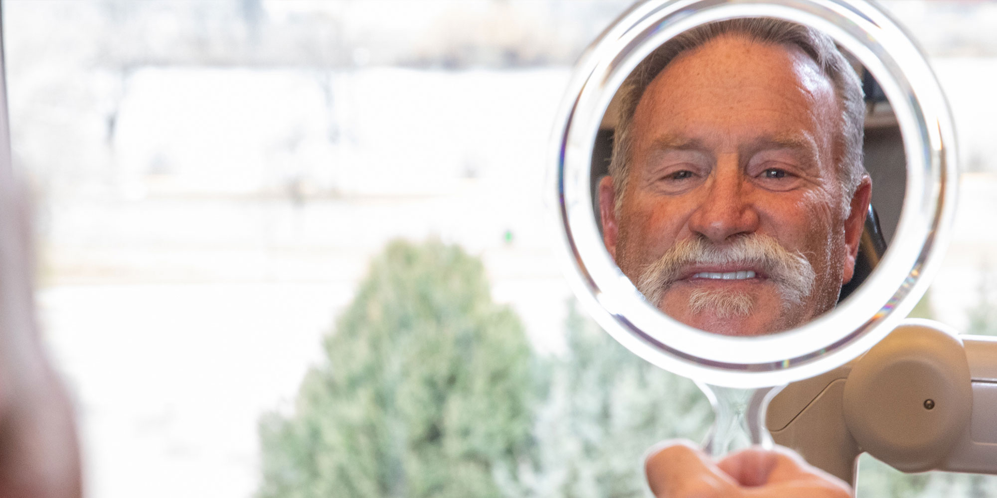 patient smiling brightly in a handheld mirror after their dental treatment